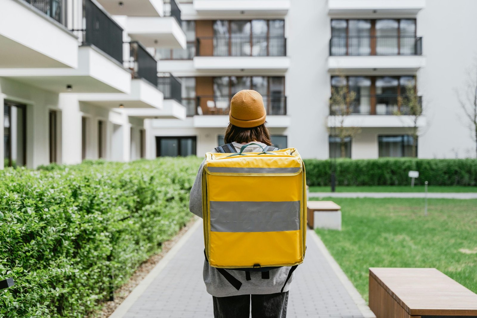 Rear view of a courier carrying a yellow delivery bag in an urban area.
